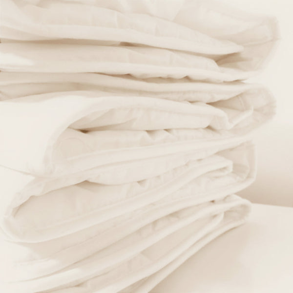 A close-up of a stack of folded white quilted bedding, showing the soft texture and stitched layers of a duvet or comforter.